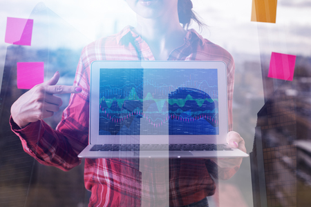 Businesswoman hand pointing at laptop with creative forex chart on blurry city background with...