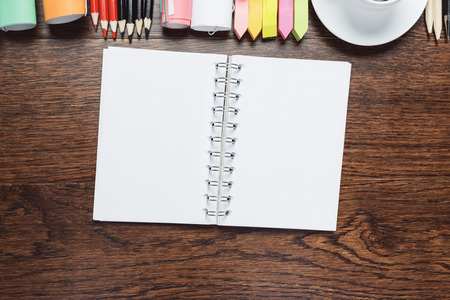 Close up of wooden office table with empty notepad, coffee cup and other items. Morning and document...