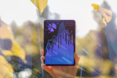 Hand holding tablet with business chart on abstract city background. Finance concept. Double...