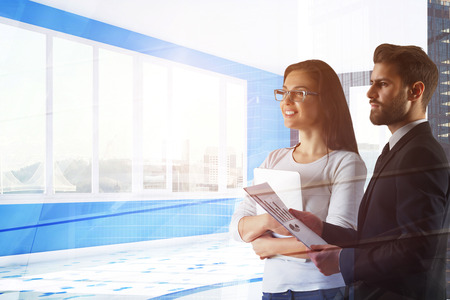 Attractive european businessman and woman standing in abstract office interior with city view. Teamwork and discussion concept. Double exposure の写真素材