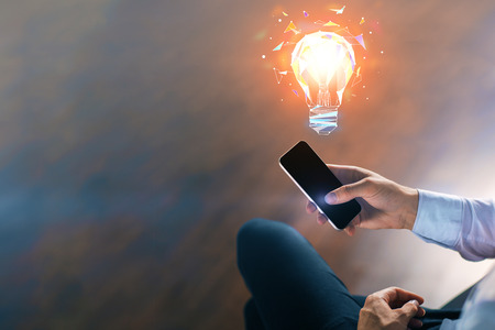 idea concept with businessman sitting with smartphone and light bulb 3d illustration at blurry abstract backgroundの写真素材