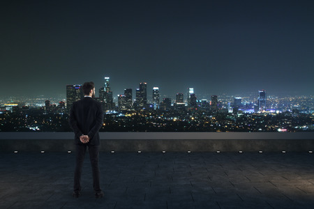 Back view of businessman on rooftop looking into the distance on night city background. Future conceptの写真素材