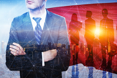Businessman with cape and folded arms standing on abstract city background with sunlight....