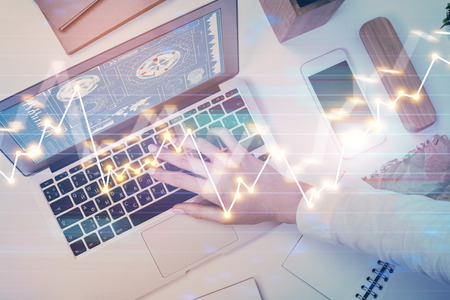 Hands typing on laptop. Business and Financial concept. Double exposure of stock market charts.