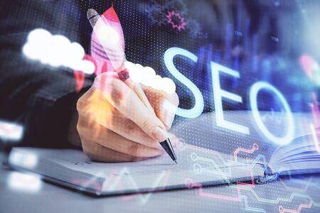 Double exposure of womans hands making notes with SEO icon. Concept of Search engine optimizationの写真素材