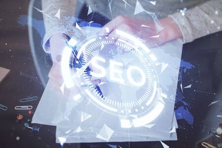 Multi exposure of womans hands making notes with SEO icon. Concept of Search engine optimizationの写真素材