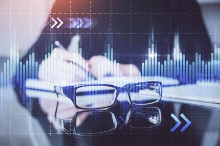 Forex chart hologram on hand taking notes background. Concept of analysis. Double exposureの写真素材
