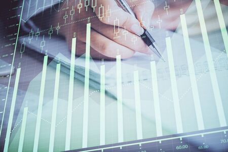 A woman hands writing information about stock market in notepad. Forex chart holograms in front. Concept of research. Multi exposureの写真素材