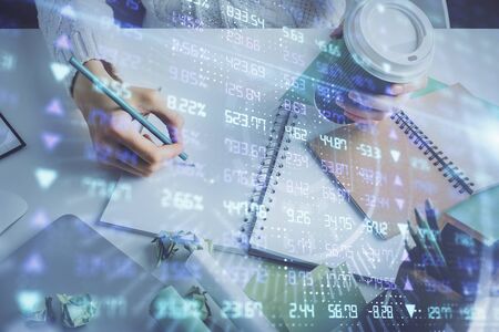 Financial forex graph displayed on hands taking notes background. Concept of research. Multi...