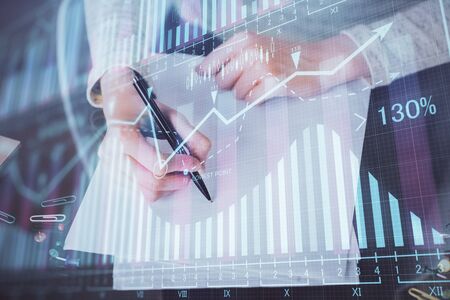 Hand taking notes in notepad. Forex chart holograms in front. Concept of research. Multi exposureの写真素材