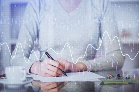 Hand taking notes in notepad. Forex chart holograms in front. Concept of research. Multi exposure