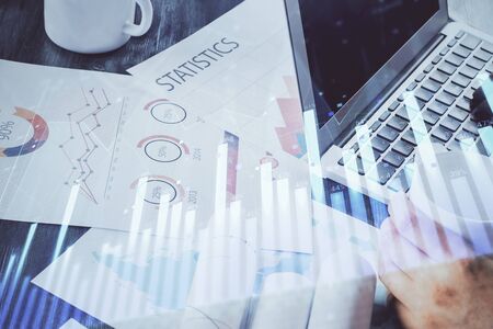 Double exposure of stock graph with businessman typing on computer in office on background. Concept...