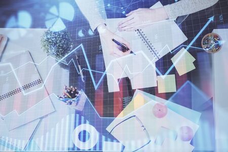Hand taking notes in notepad. Forex chart holograms in front. Concept of research. Double exposureの写真素材