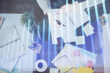 Hand taking notes in notepad. Forex chart holograms in front. Concept of research. Double exposureの写真素材