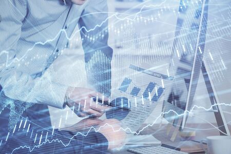 Double exposure of chart with businessman typing on computer in office on background. Concept of...