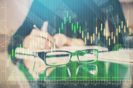 Forex chart hologram on hand taking notes background. Concept of analysis. Multi exposureの写真素材