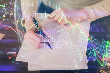 Hands macking notes in notepad. Forex chart holograms in front. Concept of research. Multi exposureの写真素材