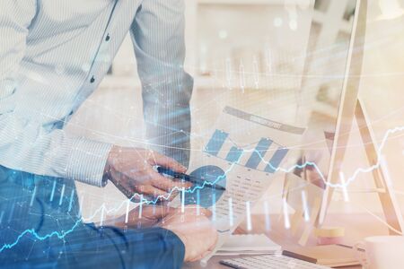 Double exposure of chart with businessman typing on computer in office on background. Concept of...