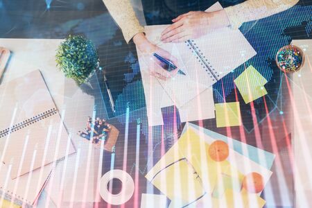 Hand taking notes in notepad. Forex chart holograms in front. Concept of research. Double exposureの写真素材