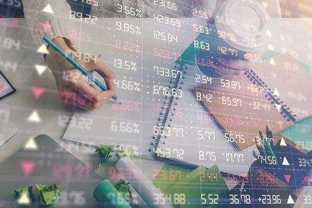 Financial forex graph displayed on hands taking notes background. Concept of research. Multi...