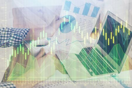Double exposure of mans hands writing notes with laptop of stock market with forex graph background. Top View. Concept of research and trading.の写真素材