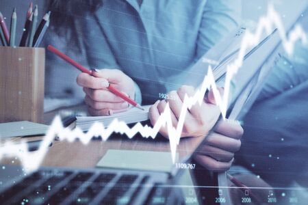 A woman hands writing information about stock market in notepad. Forex chart holograms in front. Concept of research. Multi exposureの写真素材