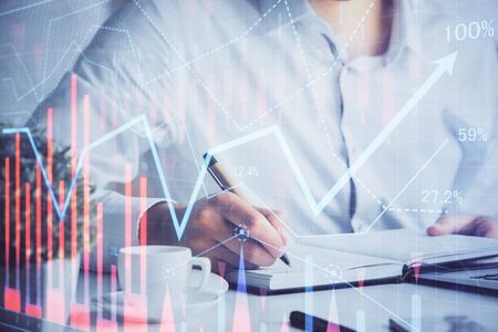 Double exposure of mans hands writing notes of stock market with forex chart.