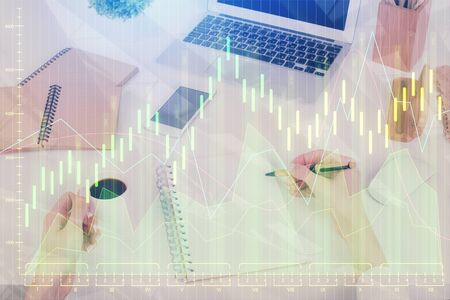 Hands writing information about stock market in notepad. Forex chart holograms in front. Concept of research. Multi exposureの写真素材