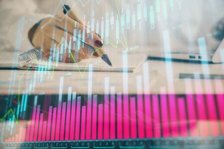 Double exposure of woman's hands making notes with forex graph hologram. Concept technical analysis.の写真素材