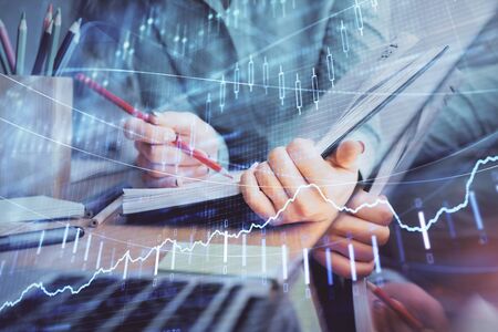 A woman hands writing information about stock market in notepad. Forex chart holograms in front....