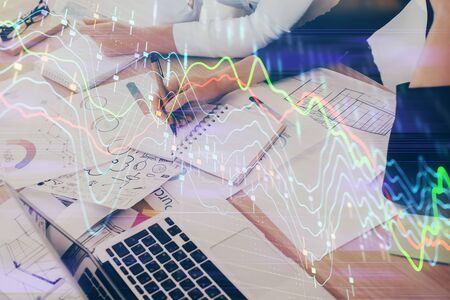 A woman hands writing information about stock market in notepad. Forex chart holograms in front. Concept of research. Double exposureの写真素材