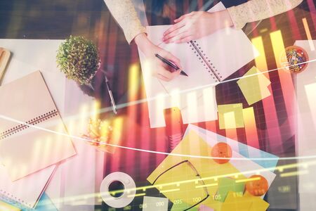 Hand taking notes in notepad. Forex chart holograms in front. Concept of research. Double exposureの写真素材