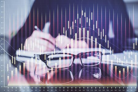 Forex chart hologram on hand taking notes background. Concept of analysis. Double exposureの写真素材