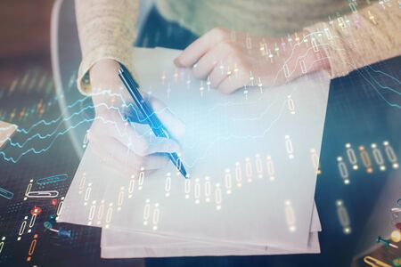 Hand taking notes in notepad. Forex chart holograms in front. Concept of research. Multi exposureの写真素材