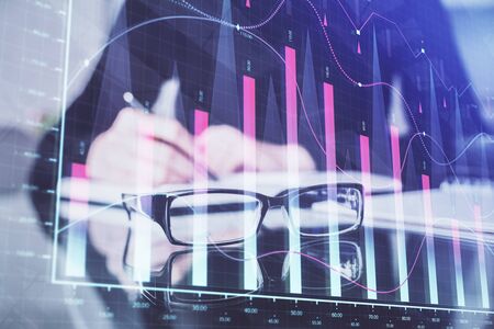 Forex chart hologram on hand taking notes background. Concept of analysis. Double exposure
