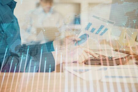 Double exposure of graph with man typing on computer in office on background. Concept of hard work. Closeup.の写真素材