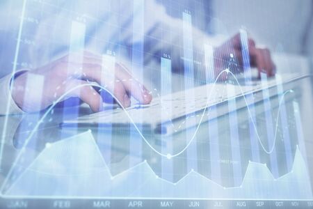 Double exposure of graph with man typing on computer in office on background. Concept of hard work. Closeup.の写真素材