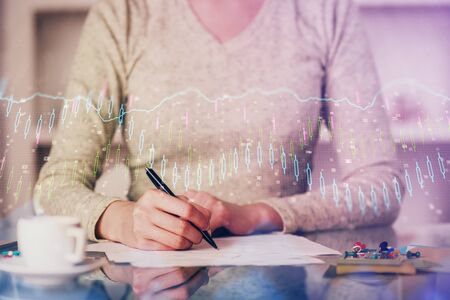 Hand taking notes in notepad. Forex chart holograms in front. Concept of research. Double exposure