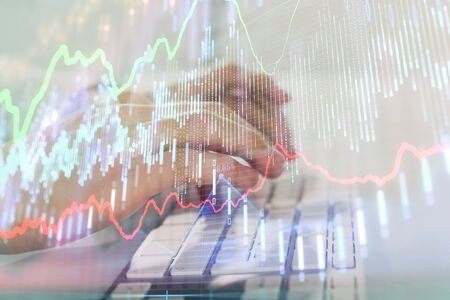 Double exposure of graph with man typing on computer in office on background. Concept of hard work. Closeup.の写真素材