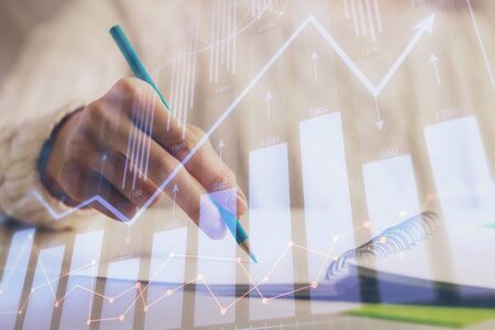 Financial forex graph displayed on hands taking notes background. Concept of research. Double exposureの写真素材