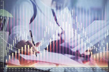 A woman hands writing information about stock market in notepad. Forex chart holograms in front. Concept of research.の写真素材