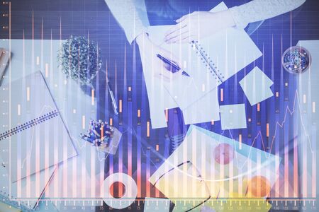 Hand taking notes in notepad. Forex chart holograms in front. Concept of research. Double exposureの写真素材