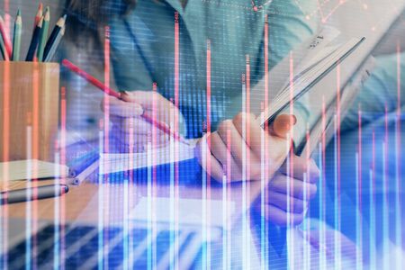 A woman hands writing information about stock market in notepad. Forex chart holograms in front....