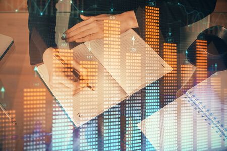 Forex chart hologram on hand taking notes background. Concept of analysis. Multi exposureの写真素材
