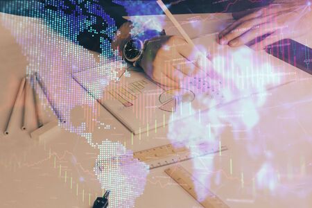 Double exposure of man's hands writing notes of stock market with forex graph background. Concept of research and trading.の写真素材