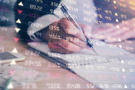 A woman hands writing information about stock market in notepad. Forex chart holograms in front....