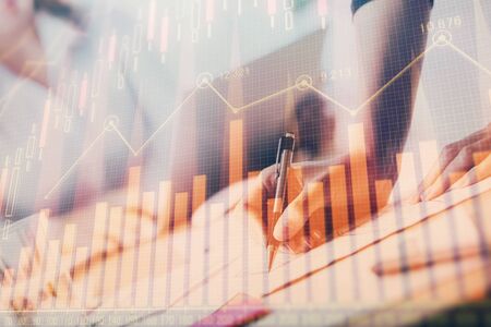 A woman hands writing information about stock market in notepad. Forex chart holograms in front....