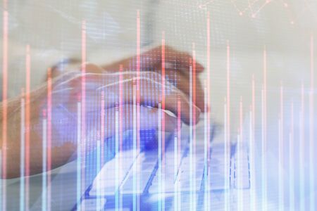 Double exposure of graph with man typing on computer in office on background. Concept of hard work....