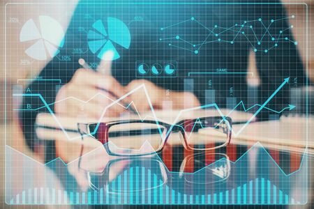 Forex chart hologram on hand taking notes background. Concept of analysis. Multi exposure