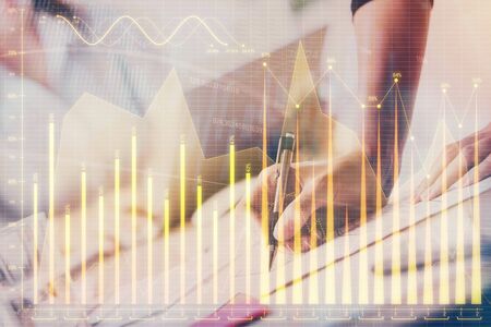 A woman hands writing information about stock market in notepad. Forex chart holograms in front....